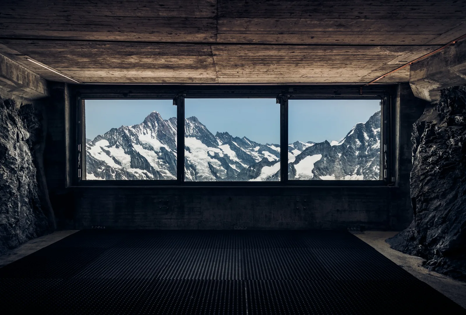 A mountain view framed by the window of a dark concrete room